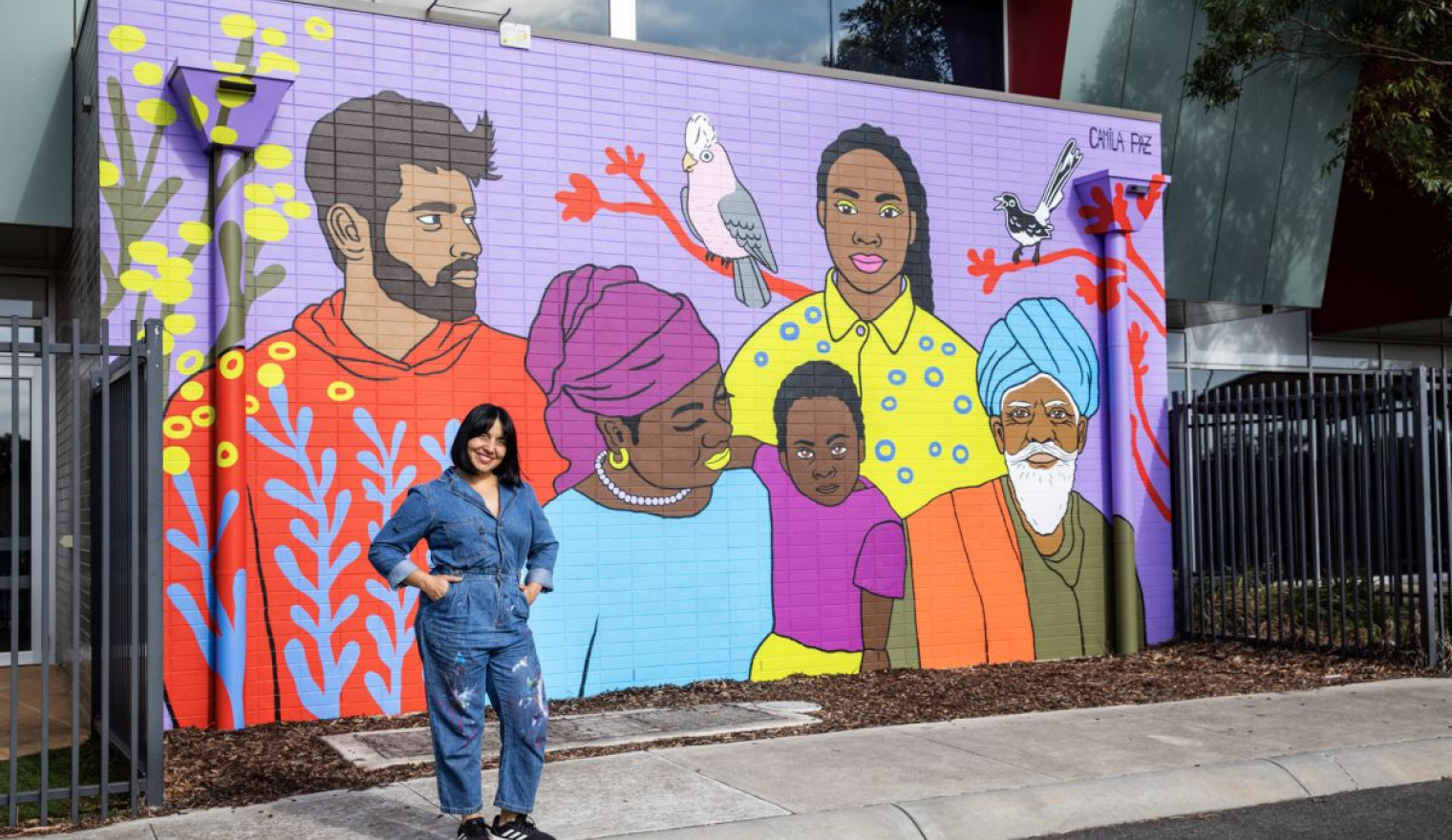 Image: Camila Paz with her commissioned mural “Whispers of the Land, Threads of Belonging” at Penrose Community Centre. Credit: Jack Gruber.