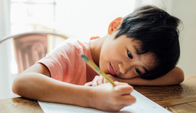 A small child leans over a paper that he is writing on