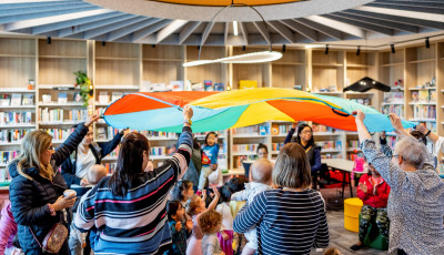 Children playing under a colourful parachute at Williams Landing lounge