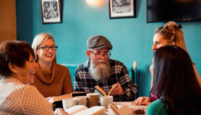 Five happy people sit around a table with hot drinks and books