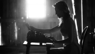 a young person with a typewriter, dramatically backlit and in black and white