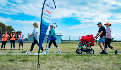 a group of adults standing on grass around a flag which says parkrun are smiling