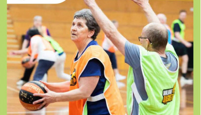 a woman wearing an orange team bib holds a basketball whilst a man wearing a green team bib stands with his hands up