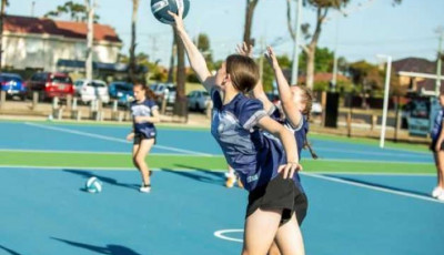 a girl reaches out to catch a ball, outside on a Netball court