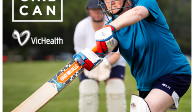 A woman wearing cricket pads and holding a cricket bat aims to hit a ball