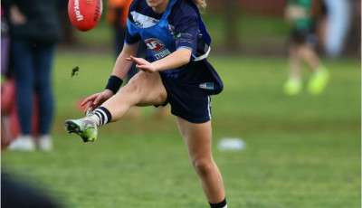 A girl wearing sports clothing kicks a red AFL ball