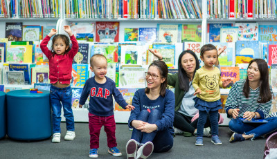 Parents sitting on the floor and children singing and dancing in the library.