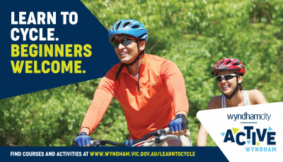 A man wearing an orange top and blue cycling helmet is cycling beside a woman wearing a red helmet