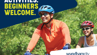 A man wearing an orange top and blue helmet and a lady wearing a red helmet cycle side by side