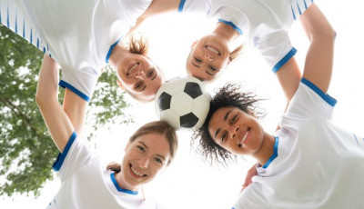 four women balance a football between their heads - view is from underneath
