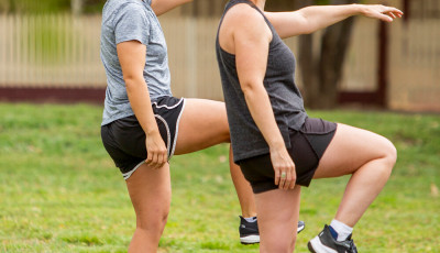 two women wearing black shorts and a grey t shirts are standing on one leg with their other knee bent and lifted