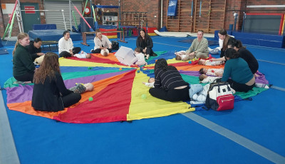a group of adults sit around a parachute with babies crawling over the parachute