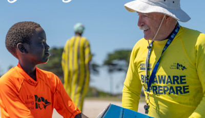 a man wearing a yellow top and white hat is talking to a boy wearing an orange top