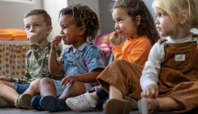 Four young children sit on the floor and practise Auslan signs.