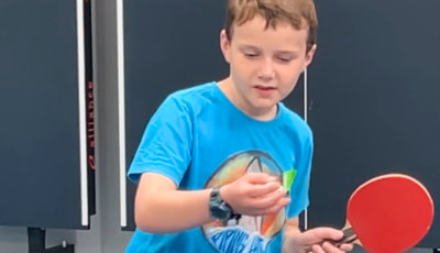 a boy in a blue t shirt is getting ready to hit a table tennis ball with a red bat