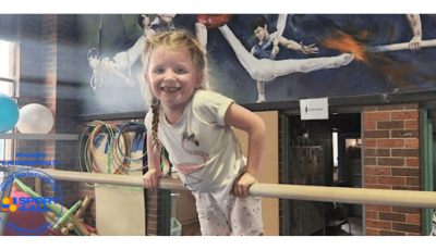 a girl is balancing on a gymnastics bar on her tummy and smiling at the camera