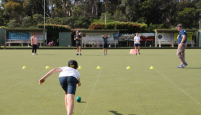 a boy is bowling down a bowling green, away from the camera