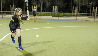 a girl wearing black sports kit is hitting a ball with a hockey stick