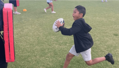 a boy holding a rugby ball is running at a tackle mat
