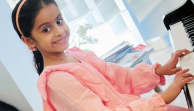 A girl playing the piano and smiling at the camera.