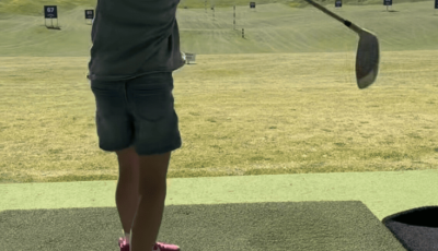 a girl wearing shorts and t shirt has just hit a golf ball into the distance with a golf club
