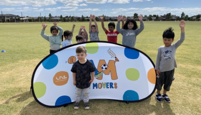 Little kids are standing around a Mini Movers sign holding up their hands