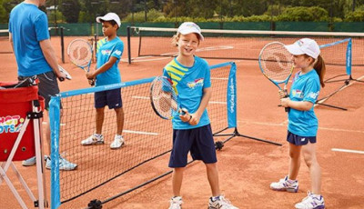 a group ok kids holding tennis rackets stand around a mini tennis net