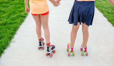 two girls holding hands are roller skating away from the camera
