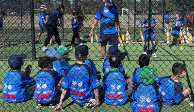 a group of boys are sitting in the cricket nets watching a coach