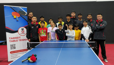 children and adults are standing behind a table tennis table and smiling at the camera