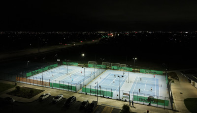 on overhead shot of 4 tennis courts with their lights and people playing Tennis