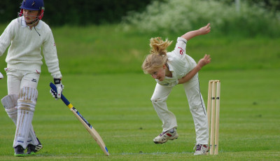 a girls has just bowled a cricket ball and a boy is getting ready to run