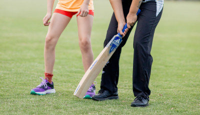 a woman is showing a child how to hold a cricket bat