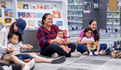 Parents and toddlers smiling and sitting together on the floor in the library.