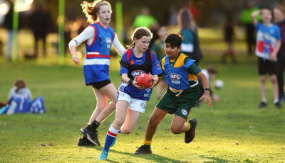 a girl is running with a Footy ball and a boy is chasing her