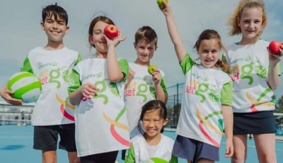 a group of kids in white and green NetSetGo T shirts are cheering at the camera