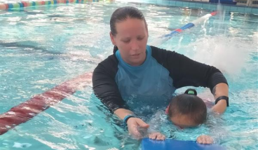 A swimming instructor is helping a child to swim with a float in the pool