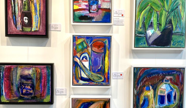Close-up photo of 6 colourful paintings by local artist James Lazaridis, displayed on a wall.